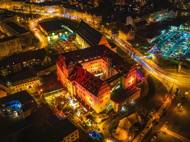 zwickau-osterstein-und-kornhaus-13-c-marko-unger.jpg Luftaufnahme von Schloss Osterstein in Zwickau bei Nacht, beleuchtet von bunten Lichtern.
