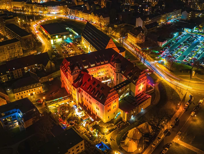 zwickau-osterstein-und-kornhaus-13-c-marko-unger.jpg Luftaufnahme von Schloss Osterstein in Zwickau bei Nacht, beleuchtet von bunten Lichtern.Aerial view of Osterstein Castle in Zwickau at night, illuminated by colorful lights.Letecký pohled na hrad Osterstein ve Zwickau v noci, osvětlený barevnými světly.Widok z lotu ptaka na zamek Osterstein w Zwickau nocą, oświetlony kolorowymi światłami.Luchtfoto van kasteel Osterstein in Zwickau bij nacht, verlicht door kleurrijke lichten.Vista aerea del castello di Osterstein a Zwickau di notte, illuminato da luci colorate.