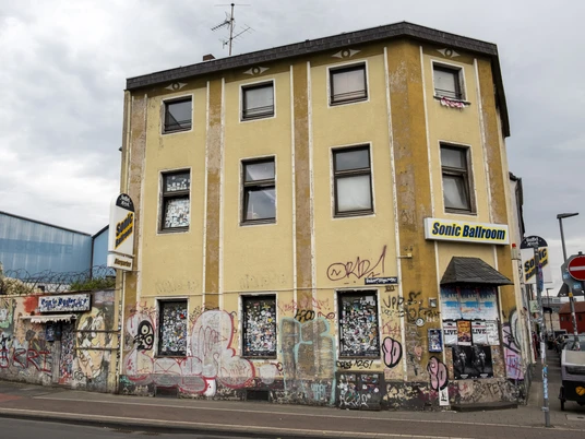 Sonic Ballroom Gelbes Haus mit grauen Dächern, urban und kreativ verziert, mit Sonic Ballroom Schriftzug.Yellow house with gray roofs, urban and creatively decorated, with Sonic Ballroom lettering.