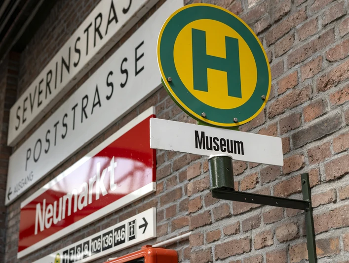 Straßenbahn-Museum Thielenbruch Straßenschilder und ein Haltestellenschild „Museum“ an einer Ziegelmauer.Street signs and a "Museum" stop sign on a brick wall.