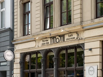 Tanoshii Fassade eines asiatischen Restaurants namens "Tanoshii" mit einer eleganten Sandsteinarchitektur, großen Fenstern und einem modernen, einladenden Design.Facade of an Asian restaurant named "Tanoshii," featuring elegant sandstone architecture, large windows, and a modern, welcoming design.