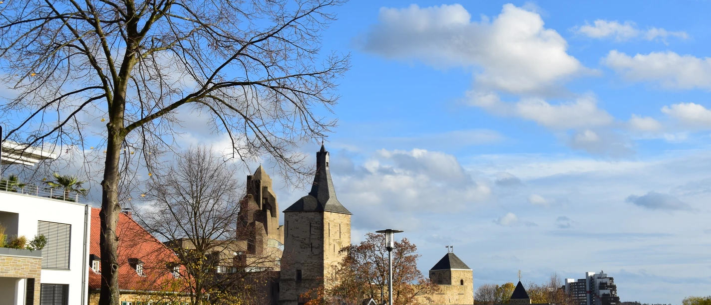 Rathaus Bensberg Ansicht von Bergisch Gladbach mit historischer Kirche und modernen Gebäuden unter blauem Himmel.