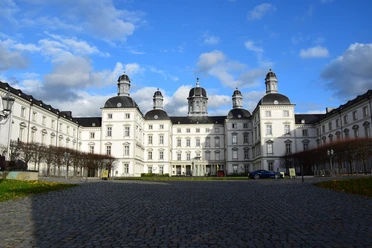 Schloss Bensberg <p>Barockes Schloss Bensberg mit weißen Fassaden und Türmen unter blauem Himmel, Kopfsteinpflaster im Vordergrund.</p>