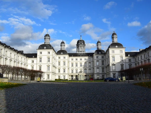 Schloss Bensberg <p>Barockes Schloss Bensberg mit weißen Fassaden und Türmen unter blauem Himmel, Kopfsteinpflaster im Vordergrund.</p>