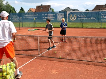Trainer, Kids, Wiese Ein Trainer steht mit zwei Kindern auf einem roten Sandtennisplatz, während sie Tennis üben.