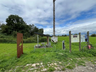 Rastplatz Windheim Rastplatz mit Tisch und Bänken unter einem Dach, umgeben von grünen Wiesen und Informationstafeln.