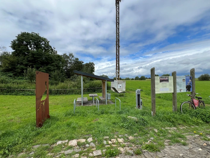 Rastplatz Windheim Rastplatz mit Tisch und Bänken unter einem Dach, umgeben von grünen Wiesen und Informationstafeln.