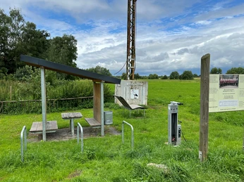 Rastplatz Windheim Rastplatz mit Überdachung und Picknicktisch inmitten einer grünen Wiese unter bewölktem Himmel.
