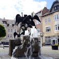 Gänsemarkt_2011_Siwinski_4.jpg Ein Brunnen mit Gänsestatuen vor historischen Gebäuden bei sonnigem Wetter auf einem Platz.
