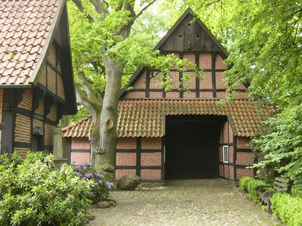 Haus Tiding Historisches Fachwerkhaus mit rotem Ziegeldach, umgeben von Bäumen und blühenden Sträuchern