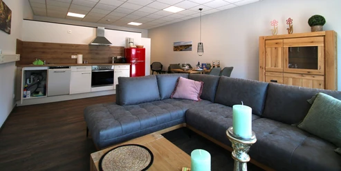 FeWo thelivingroom-wohnbereich.jpg Moderner Wohnbereich mit offener Küche, gemütlicher Couch und stilvollen Dekorationselementen im Raum.