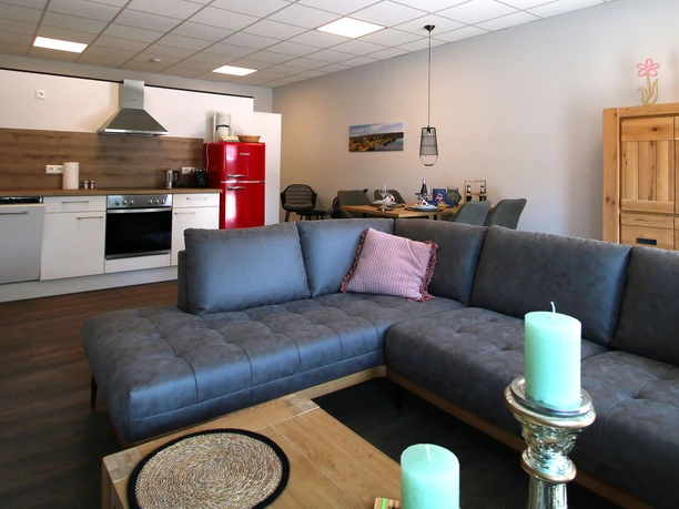 FeWo thelivingroom-wohnbereich.jpg Moderner Wohnbereich mit offener Küche, gemütlicher Couch und stilvollen Dekorationselementen im Raum.