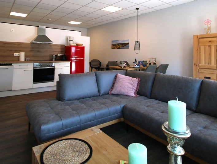 FeWo thelivingroom-wohnbereich.jpg Moderner Wohnbereich mit offener Küche, gemütlicher Couch und stilvollen Dekorationselementen im Raum.