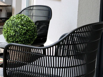 Zwei schwarze Rattansessel mit grauen Polstern und einer Dekokugel auf einer Terrasse.