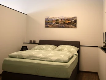 Schlafbereich mit Doppelbett in moderner Ferienwohnung, helle Wände, ruhige Atmosphäre, Wandkunst.