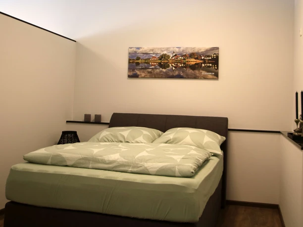 Schlafbereich mit Doppelbett in moderner Ferienwohnung, helle Wände, ruhige Atmosphäre, Wandkunst.