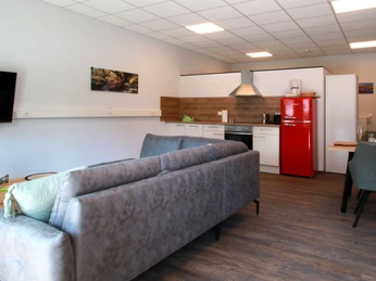 FeWo-thelivingroom-wohnbereich-flur.jpg Moderner Wohnbereich einer Ferienwohnung mit Sofa, Couchtisch, Küche, Esstisch und roten Kühlschrank.