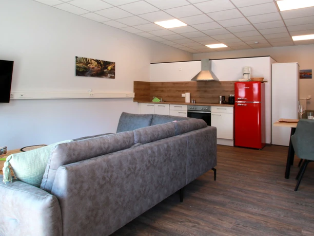 FeWo-thelivingroom-wohnbereich-flur.jpg Moderner Wohnbereich einer Ferienwohnung mit Sofa, Couchtisch, Küche, Esstisch und roten Kühlschrank.
