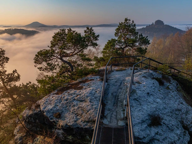 Rocky plateau with viewing platform, surrounded by fog, trees and vast landscape in the background.
