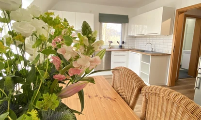 Die Küche in der Fewo-Neandersteig in Heiligenhaus Helle Küche in Heiligenhaus mit Esstisch, Korbstühlen, Blumenarrangement und moderner Ausstattung.
