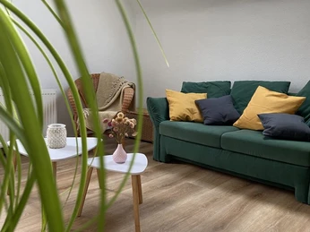 Wohnbereich in der Fewo-Neandersteig in Heiligenhaus Moderner Wohnbereich in einer Ferienwohnung mit grüner Couch, Holzboden, hellem Tisch und Sessel.