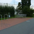 P1110201.JPG Ruhiger Rastplatz mit Metallbank und Fahrradständern auf einer gepflasterten Fläche neben einem Weg.