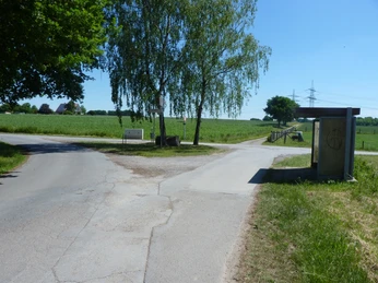 P1110091.JPG Ländliche Kreuzung mit Wegweiser, Bushaltestelle, umgeben von grünen Feldern und Bäumen.