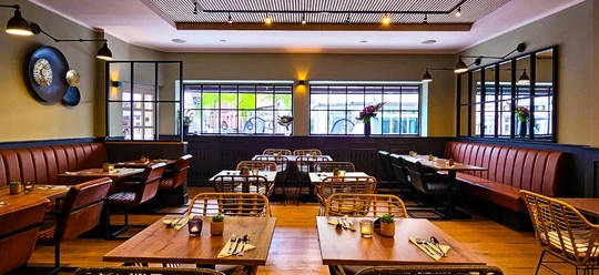 Chans Thai Kitchen Ruhiges Restaurant mit modernen Holztischen, Stühlen und großen Fenstern, die Tageslicht hereinlassen.
