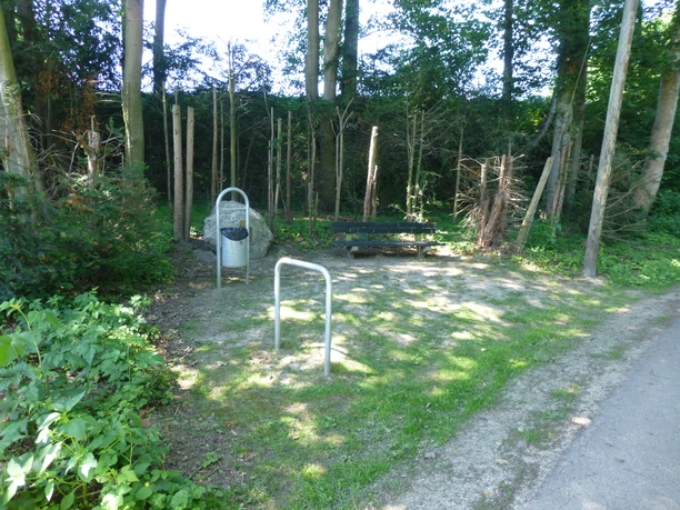 P1120364.JPG Grüne Parkbank im Schatten, umgeben von Bäumen, daneben ein Abfalleimer und ein Fahrradständer.