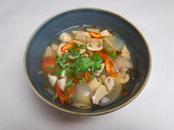 Eine Schale asiatische Suppe, gefüllt mit Pilzen, Zwiebeln, Tomaten und frischen Kräutern, serviert.