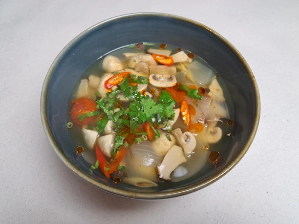 Eine Schale asiatische Suppe, gefüllt mit Pilzen, Zwiebeln, Tomaten und frischen Kräutern, serviert.