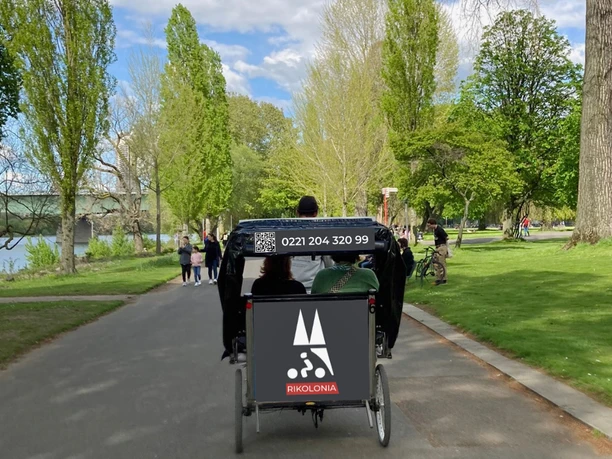 Rikolonia Eine Rikscha fährt durch einen grünen Park in Köln, gehüllt in ein klares Frühlingslicht.