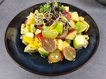 24 Yam Polamei.jpg Frischer Obstsalat mit Trauben, Äpfeln, Drachenfrucht, Mais und Microgreens, serviert auf einem Teller.