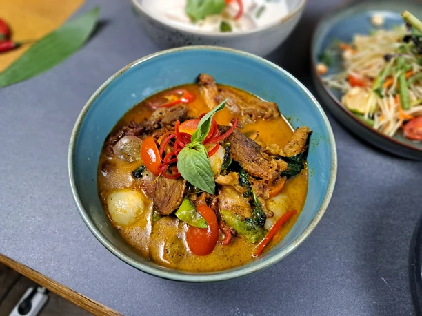 20231115_200757.jpg Eine blaue Schale mit würzigem Curry enthält Rindfleischstücke, Paprika, Basilikum und Gemüse.