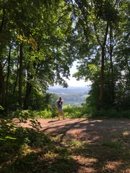 Burgweg mit Brockenblick Eine Wanderin steht auf einem Waldweg und blickt über das grüne Tal zum Brocken in der Ferne.