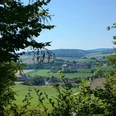 Burgweg Taubergsruh Blick durch Bäume auf grüne Felder und ein Dorf im Tal bei Einbeck unter blauem Himmel.