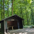 Burgweg-Hube - Schwarze Hütte Holzhütte mit Satteldach und Rastbank im grünen Laubwald am Burgweg in der Hube bei Einbeck