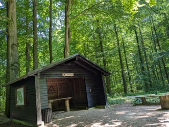 Schwarze Hütte auf der Hube Holzhütte mit Satteldach und Rastbank im grünen Laubwald am Burgweg in der Hube bei Einbeck