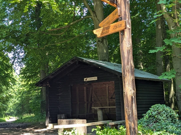Burgweg Hube - Schwarze Hütte Holzhütte im Wald mit Rastplatz und Wegweiser, von Sonnenlicht durch das Blätterdach beleuchtet.