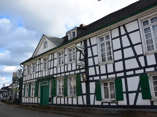 Fachwerk in Witzhelden Fachwerkhaus in Leichlingen mit grün-weißer Fassadengestaltung, historische Architektur bei Wolkenhimmel.