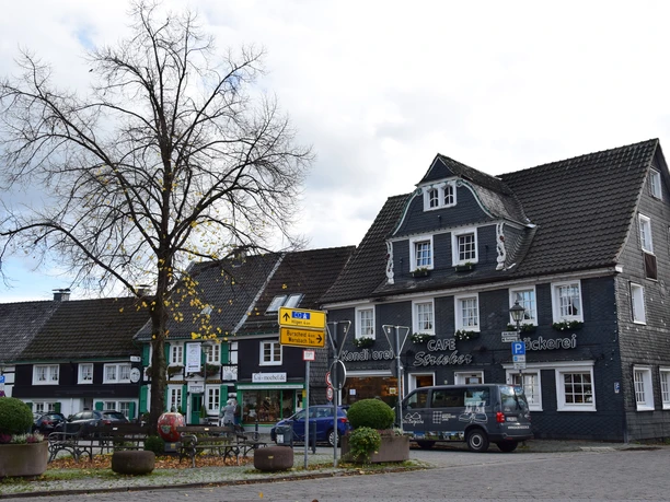 Ortskern Witzhelden Fachwerkhausplatz in Leichlingen mit Café, Bäckerei, herbstlichem Baum und parkendem Lieferwagen.