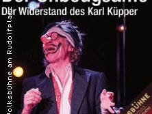 Karl Küpper in Clownskostüm mit roter Nase und Sonnebrille, lächelt bei Bühnenshow vor schwarzem Hintergrund.