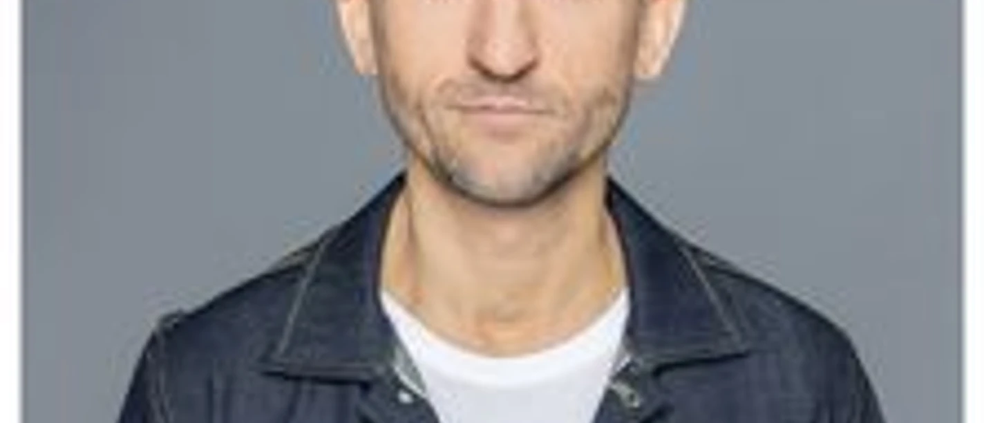 Markus Barth lächelt leicht in die Kamera, vor grauem Hintergrund, in Jeansjacke und weißem Shirt.