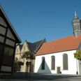 DSC_0545.JPG Fachwerkhaus, Kirche mit rotem Ziegeldach und Turm, umgeben von gepflastertem Platz und Bäumen.