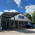ALDI.jpg Ein ALDI-Supermarkt mit Backsteinfassade. Vor dem Gebäude stehen mehrere Autos. Der Himmel ist blau mit Wolken.