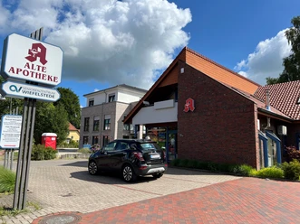 Alte Apotheke.jpg Das Bild zeigt eine rote Backsteingebäude, das die "Alte Apotheke" ist, mit einem markanten Eingang und einem daneben stehenden Auto.