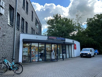 Apotheke Wiefelstede im Ärztezentrum.jpg Die Apotheke Wiefelstede im Ärztezentrum hat eine moderne Glasfront und einen Eingang, der von einem Vordach geschützt ist. Vor dem Gebäude stehen Fahrräder und ein Auto. Über der Tür befindet sich ein Schild mit dem Namen der Apotheke.