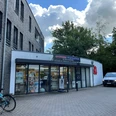 Apotheke Wiefelstede im Ärztezentrum.jpg Die Apotheke Wiefelstede im Ärztezentrum hat eine moderne Glasfront und einen Eingang, der von einem Vordach geschützt ist. Vor dem Gebäude stehen Fahrräder und ein Auto. Über der Tür befindet sich ein Schild mit dem Namen der Apotheke.