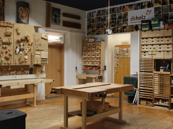 KreativWerkstatt am Wall Holzwerkstatt mit Werkbänken, geschnitzten Kunstwerken und fertigen Holzstücken an den Wänden.