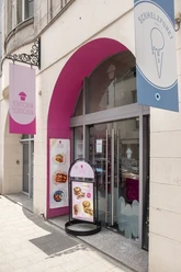 Törtchen Törtchen Die Fassade von "Törtchen Törtchen" in Köln mit einem großen, pinken Bogen und einladendem Schaufenster.